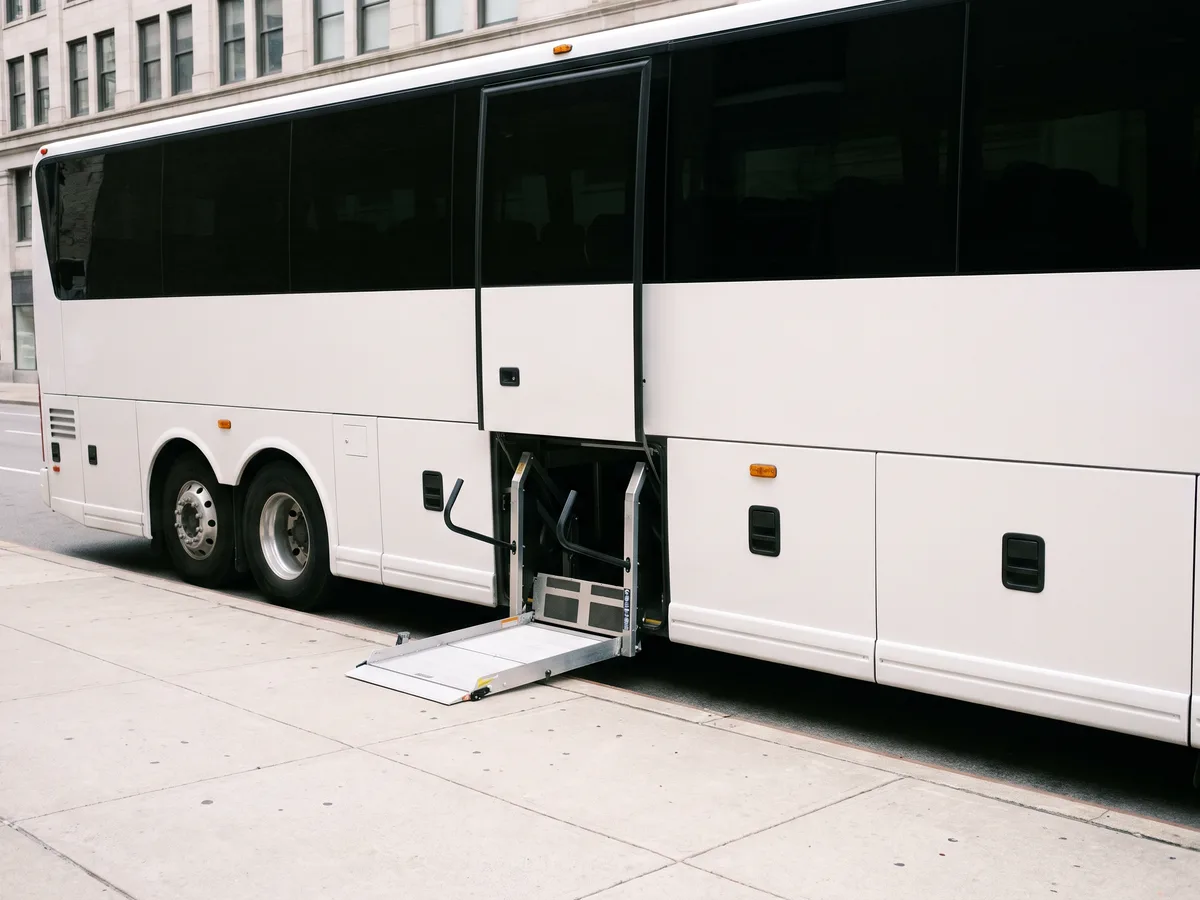 A wheelchair lift lowered from the side door of a white coach bus to the curb