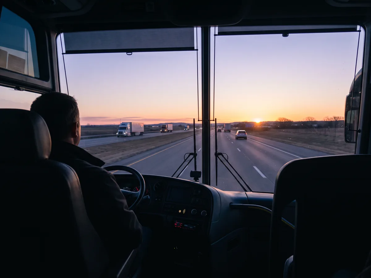 The view past a coach bus driver's shoulder down a highway at sunrise