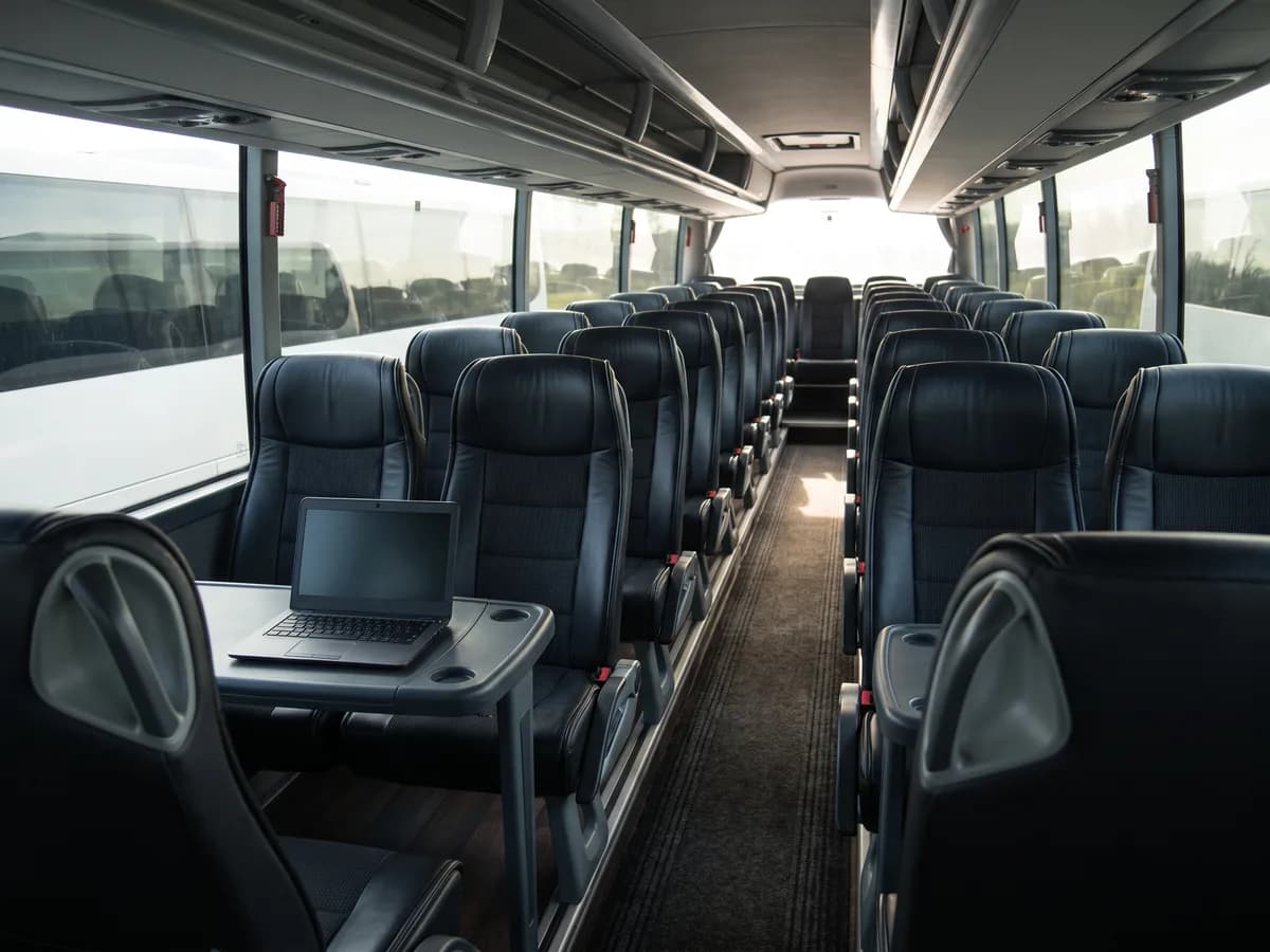 Leather seats inside a coach bus, with a laptop on a fold-down tray