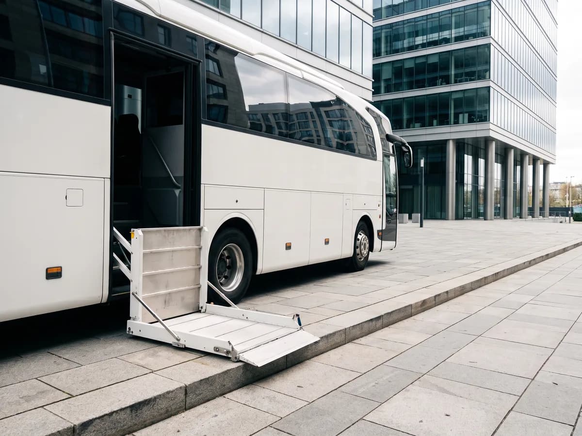 A coach bus's wheelchair lift lowered to the curb in front of modern glass office buildings