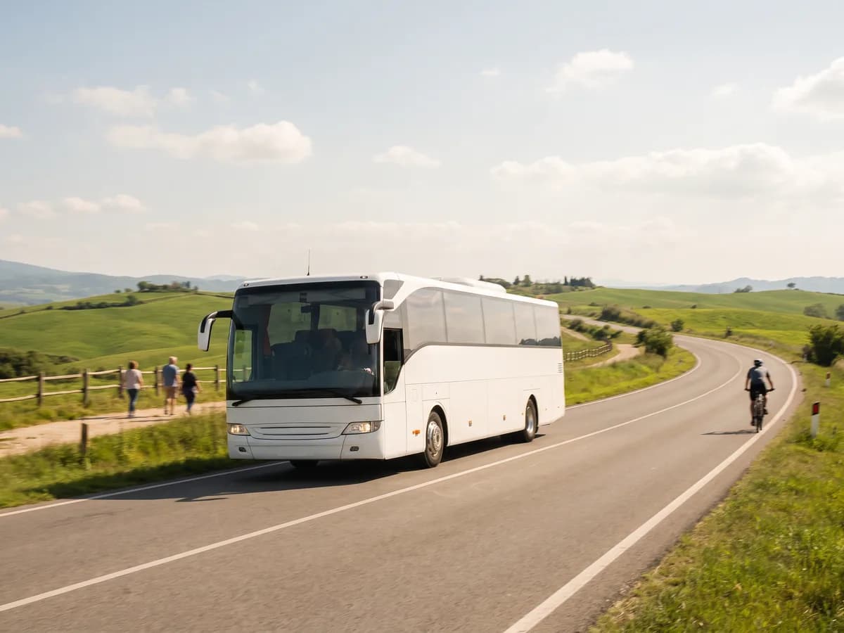A white coach bus on a two-lane road winding through green rolling hills