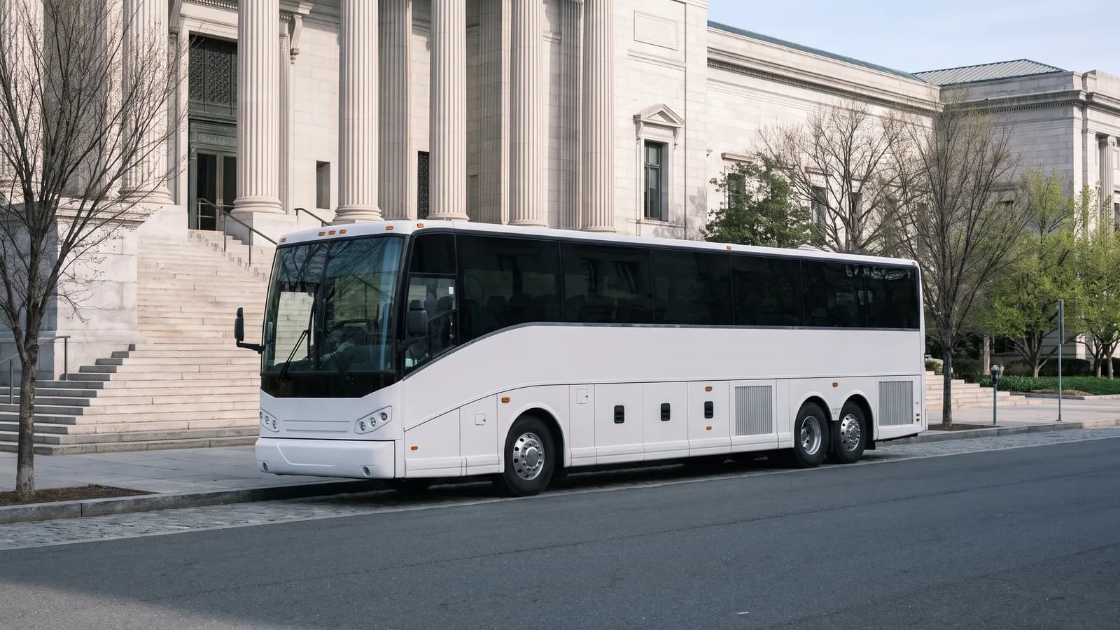 A white coach bus parked at the curb in front of a museum with wide stone steps and columns