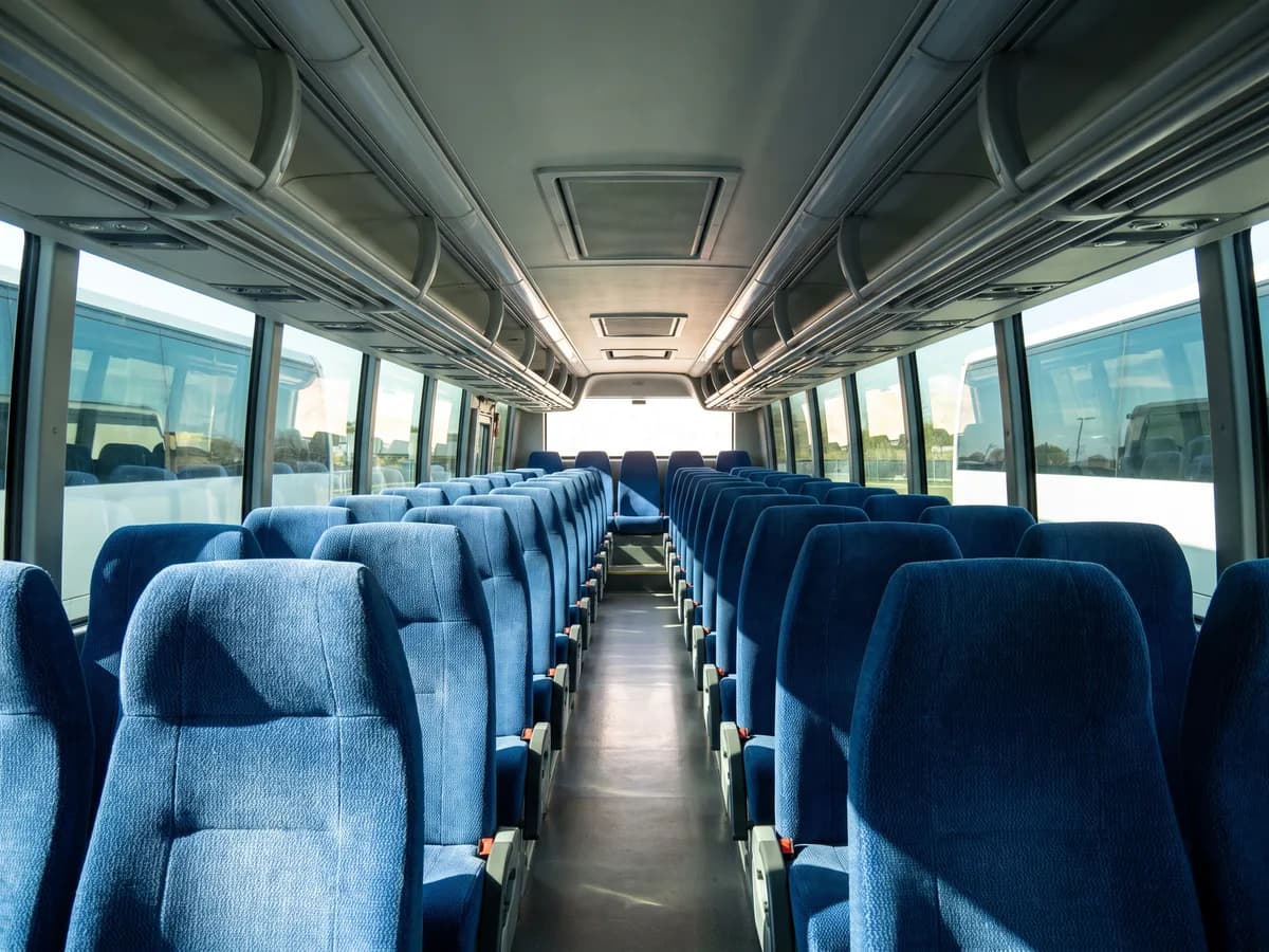 Rows of empty blue seats inside a coach bus in bright daylight