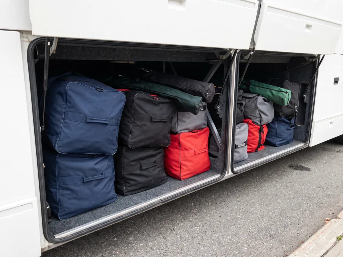 Navy, black and red equipment bags packed into the under-floor luggage bay of a coach bus