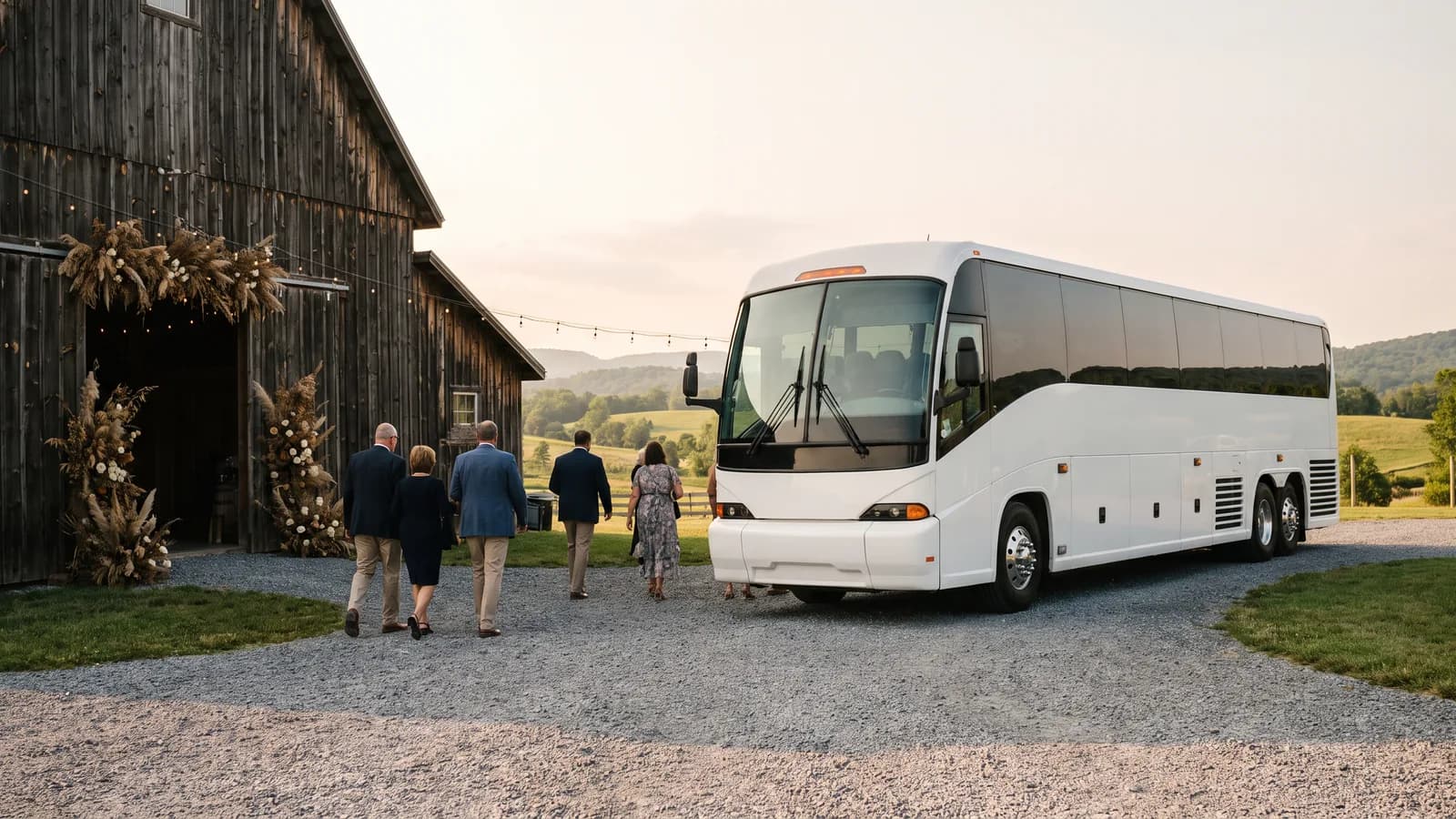 Wedding guests walking toward a white coach bus parked beside a rustic barn venue