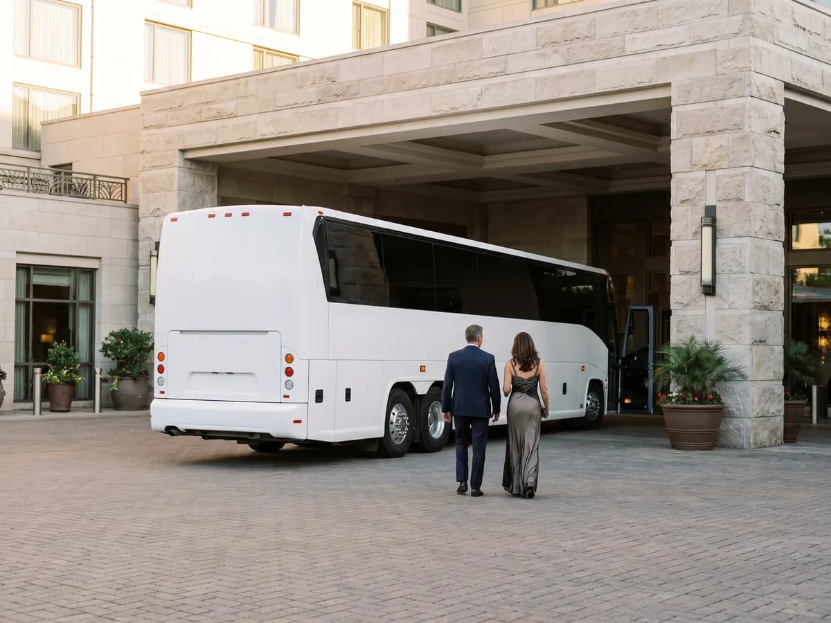 Two wedding guests in formal clothes walking toward a coach bus at a hotel entrance